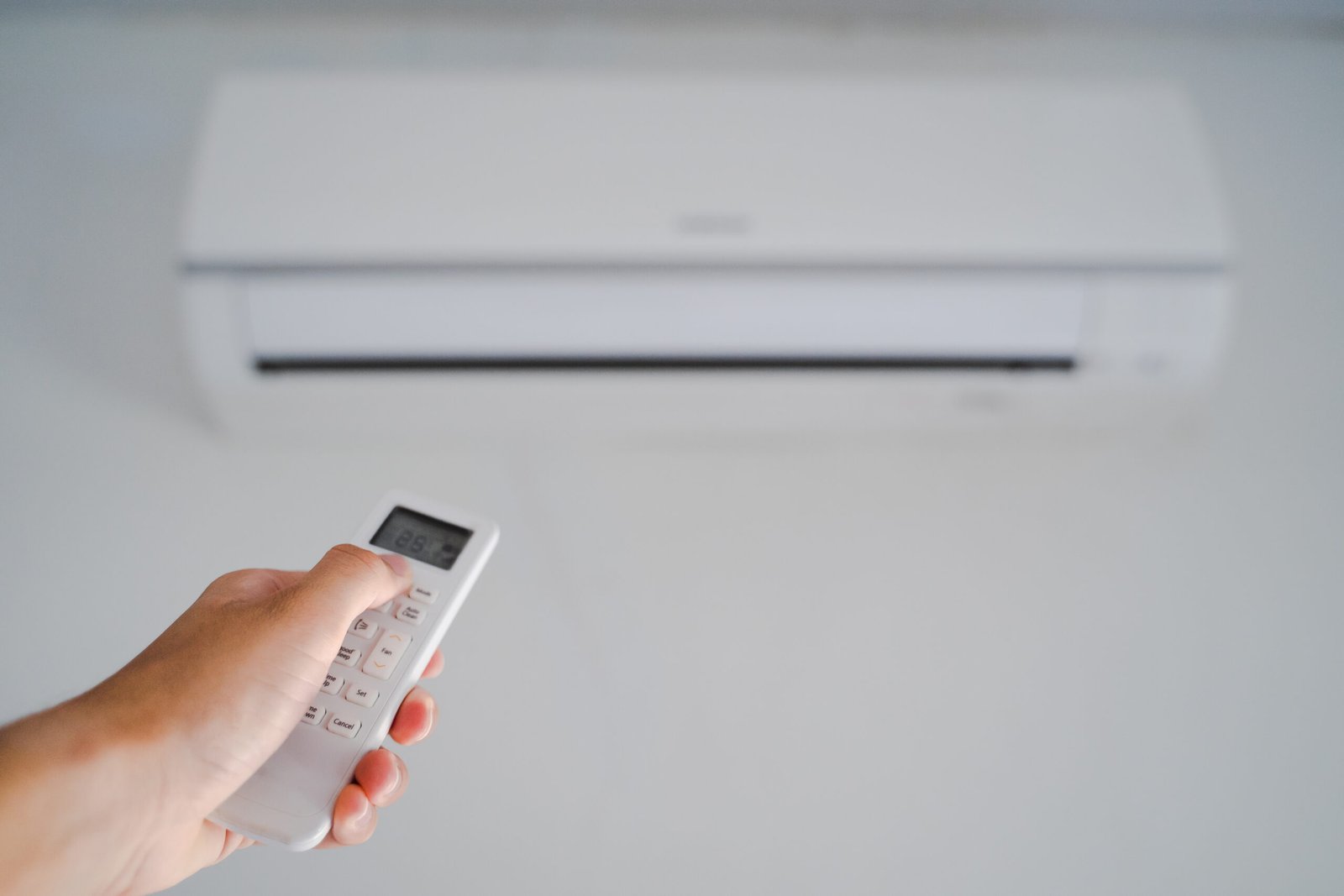 Man hand operating remote controller the air conditioner inside the room.